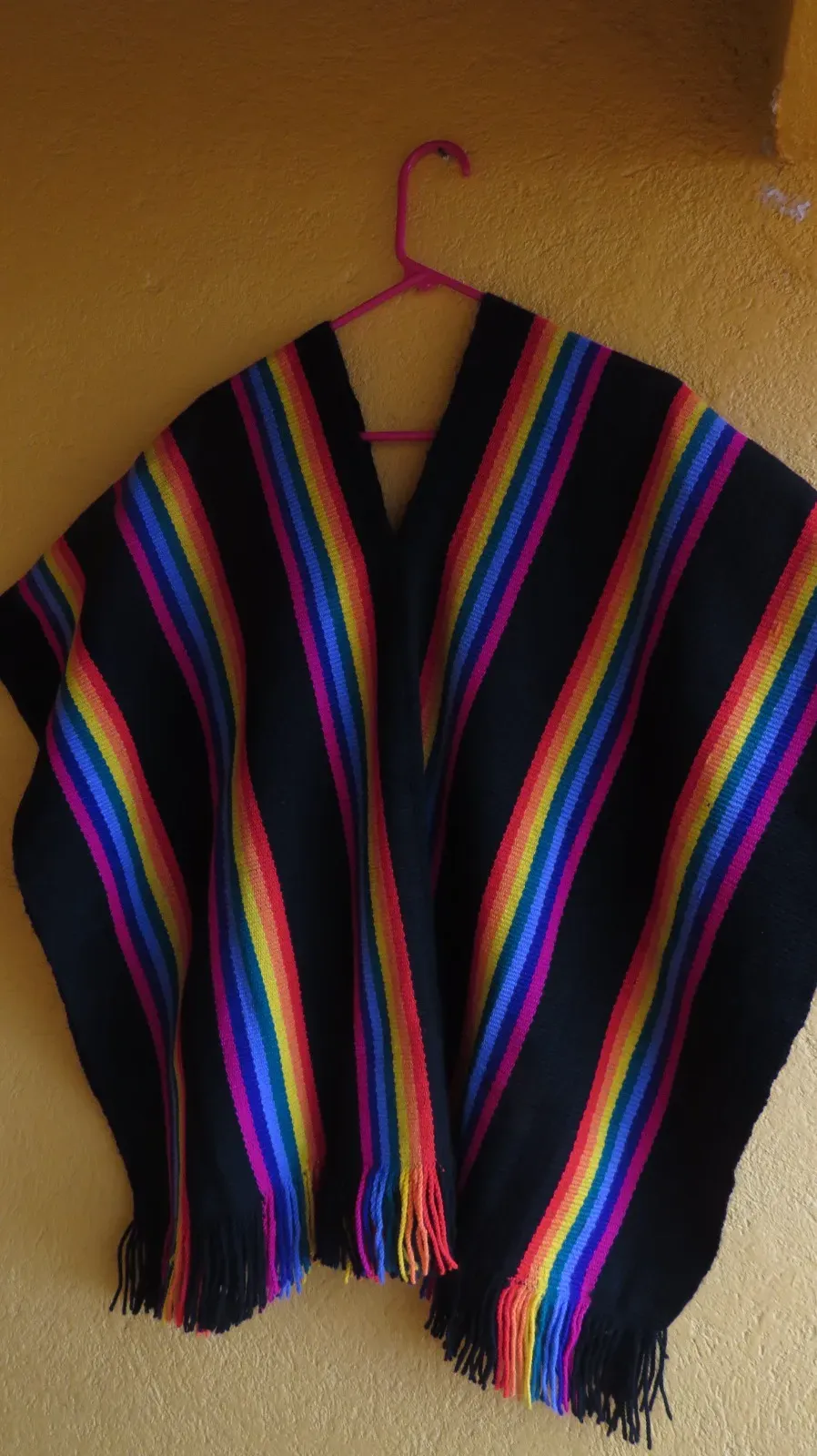 Poncho negro con franjas de colores y flecos, colgado